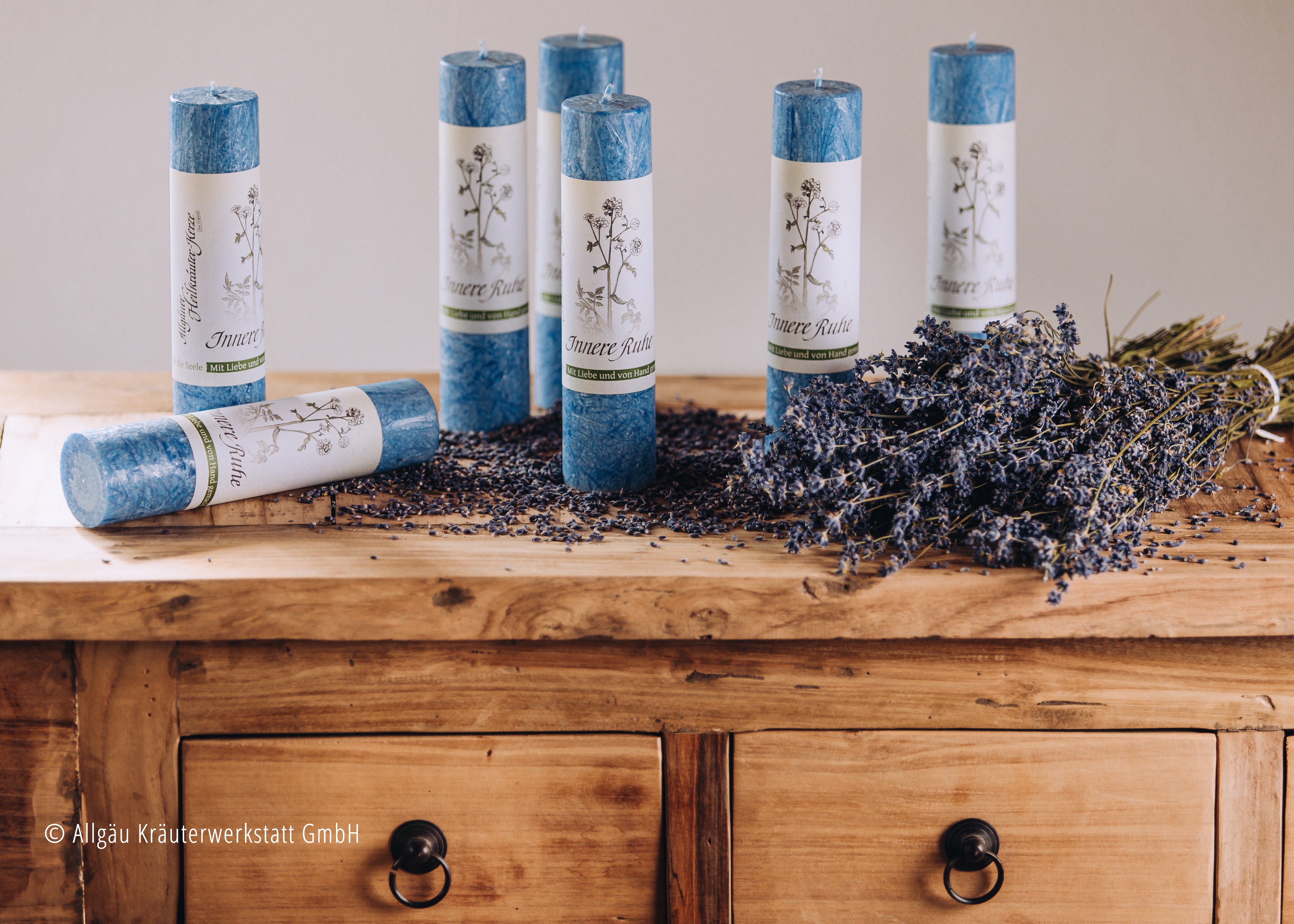 Mehrere Kerzen in blau auf einer alten Holzkommode dekoriert mit Lavendelblüten