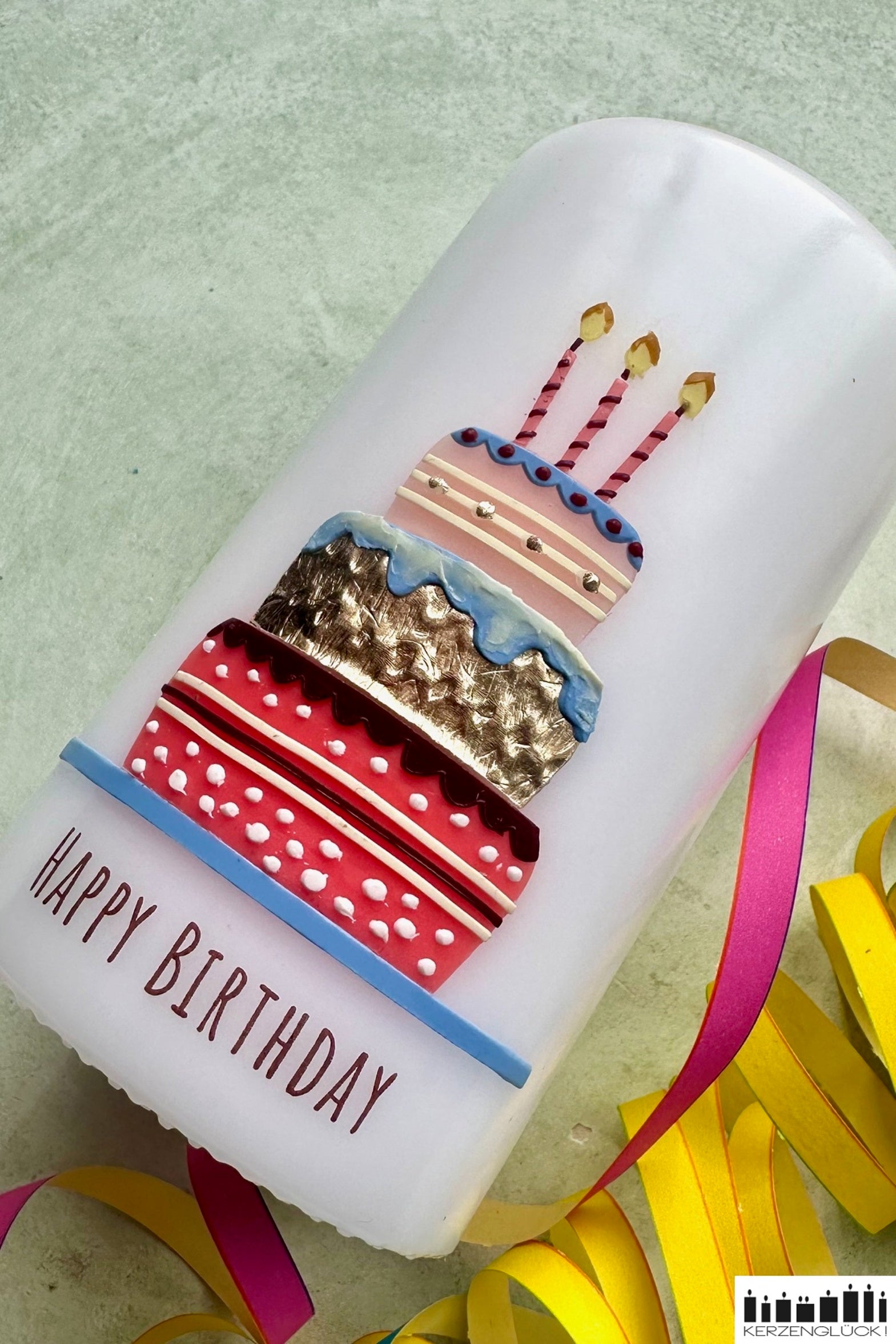 Eine Geburtstagskerze mit Torte und Kerzen verziert auf einer hellen Unterlage umrandet von Luftschlangen