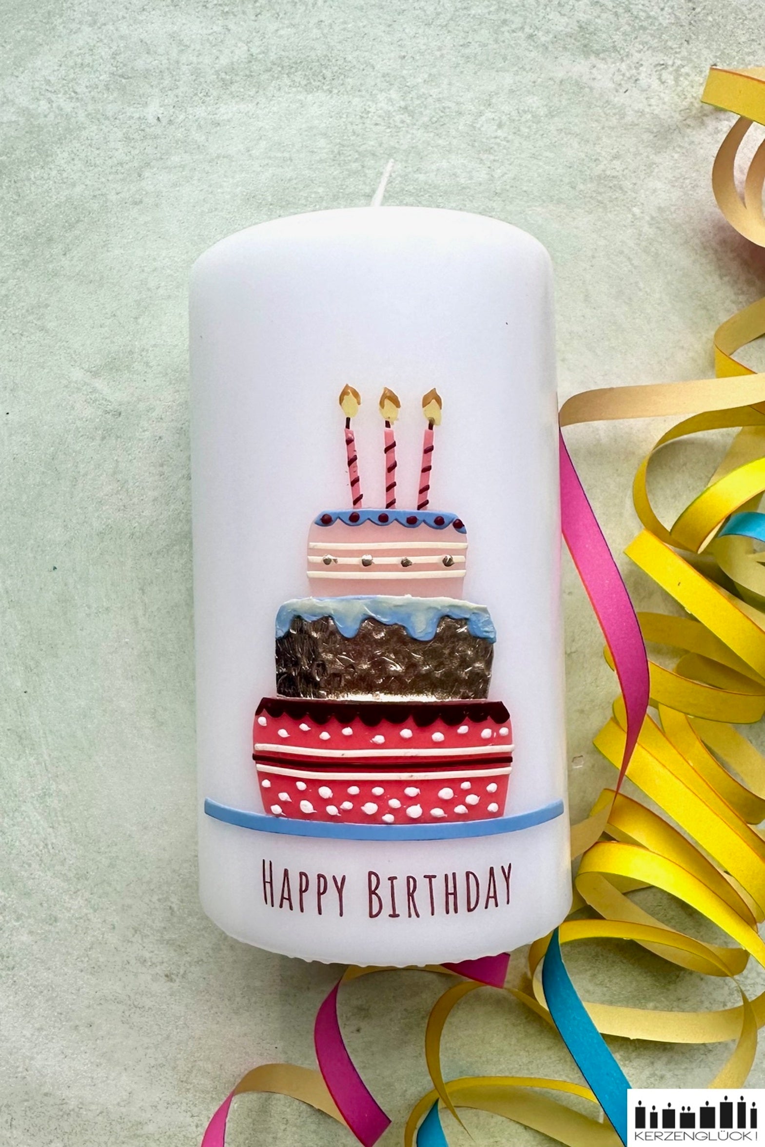Eine Geburtstagskerze mit Torte und Kerzen verziert auf einer hellen Unterlage umrandet von Luftschlangen