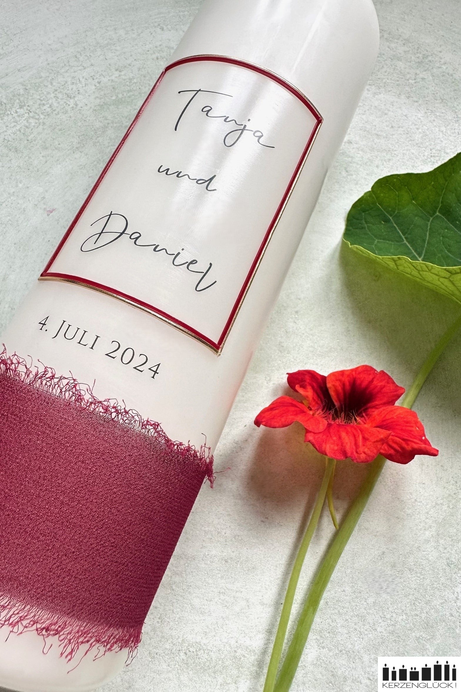 Nahaufnahme von Hochzeitskerze Frame in weinrot neben einer Blüte