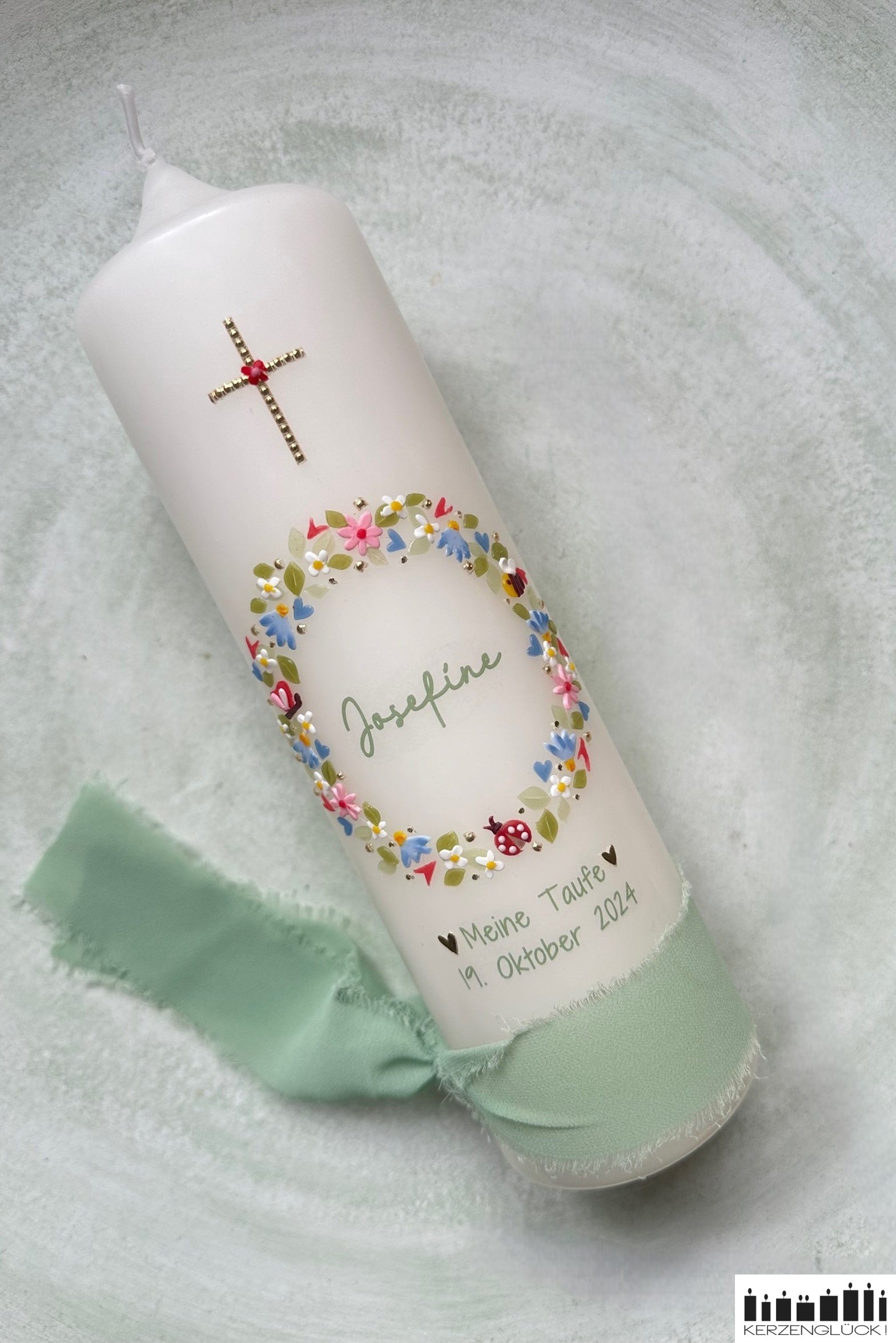 Taufkerze diagonal liegend auf hellem Untergrund mit lindgrünem Seidenband