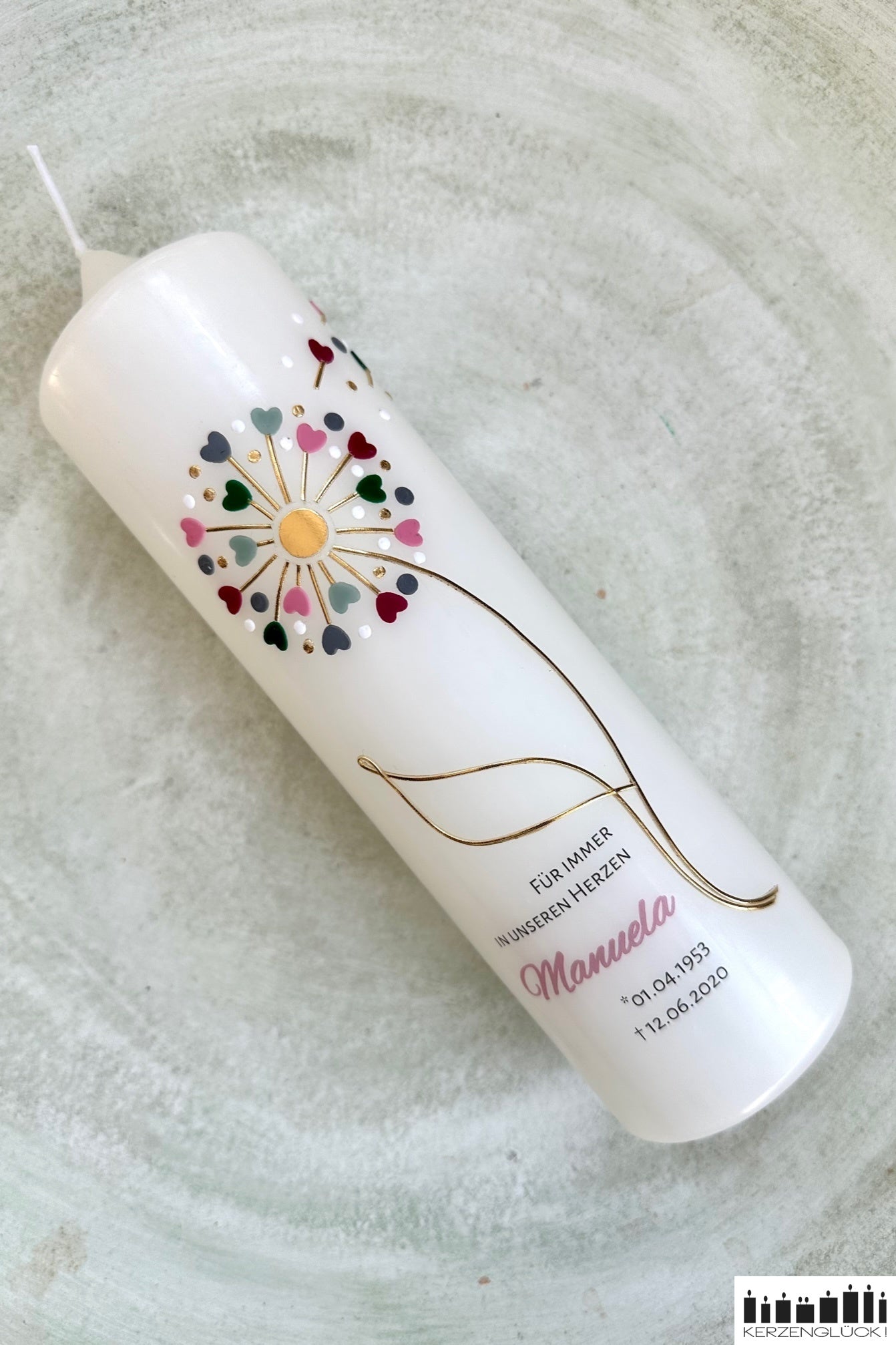 Trauerkerze Pusteblume diagonal auf einem hellen Teller liegend, ganze Kerze in der Übersicht