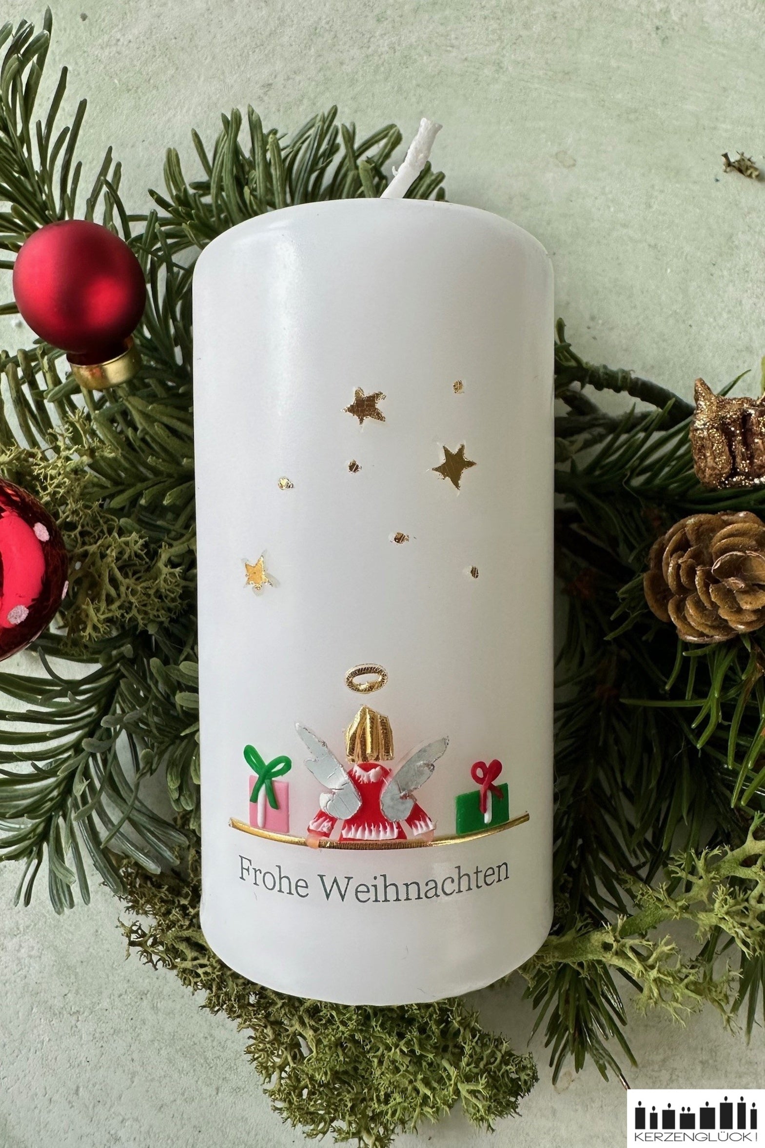 Weihnachtskerze Engel auf Tannenzweigen liegend und mit roten Glaskugeln und Zapfen dekoriert