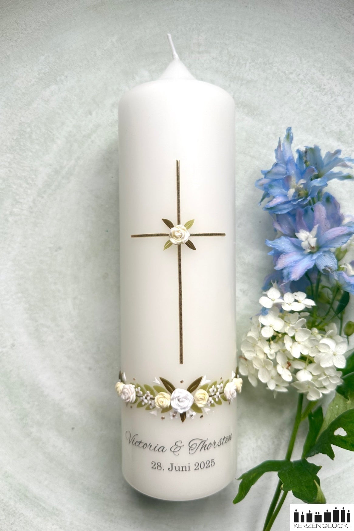 Hochzeitskerze mit weißen Rosen und goldenem Kreuz mit Blumen dekoriert