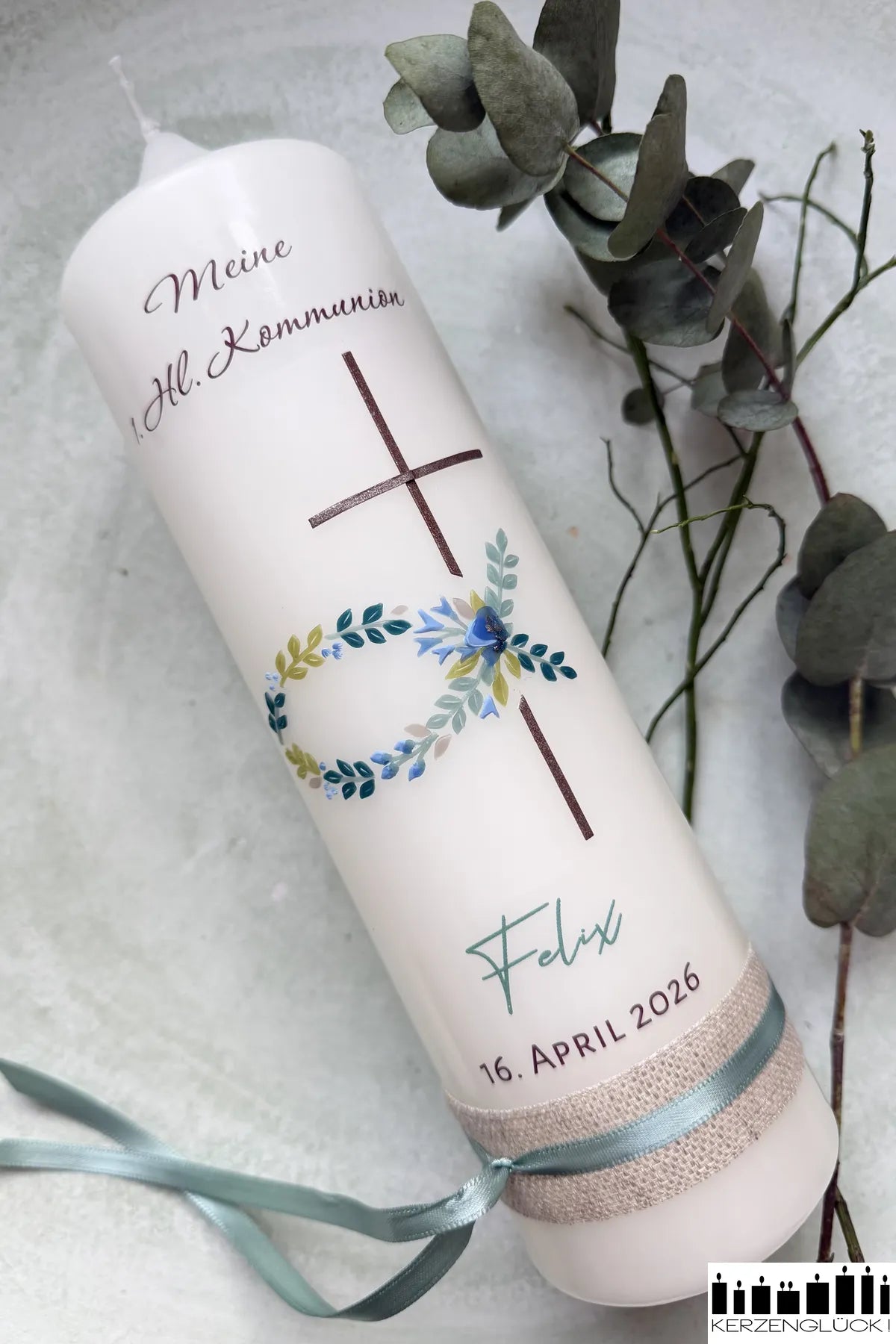 Kommunionkerze Fisch mit Kreuz auf hellem Untergrund liegend und mit Blättern dekoriert