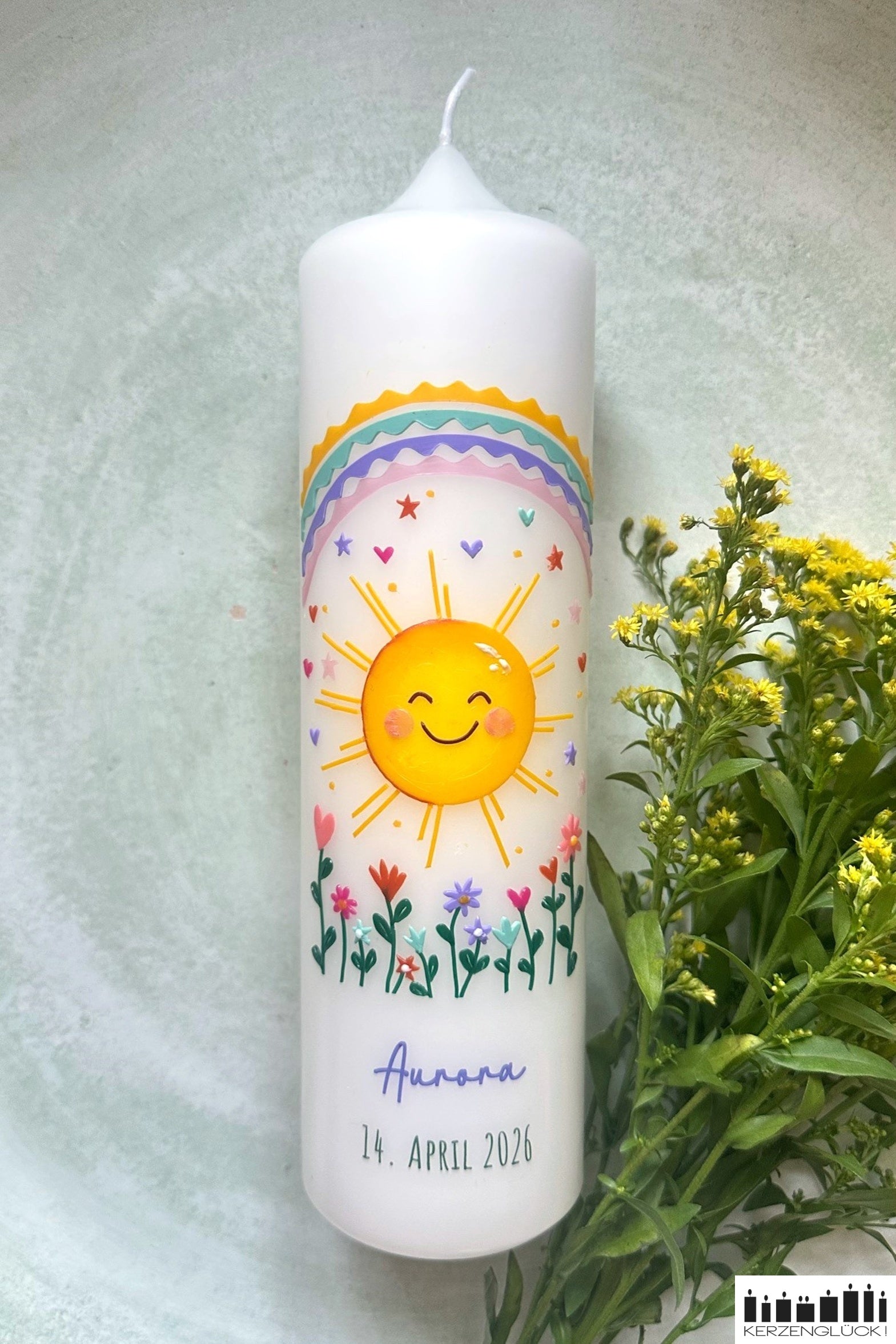 Taufkerze Sonne liegend auf hellem Untergrund mit Blumedekoration