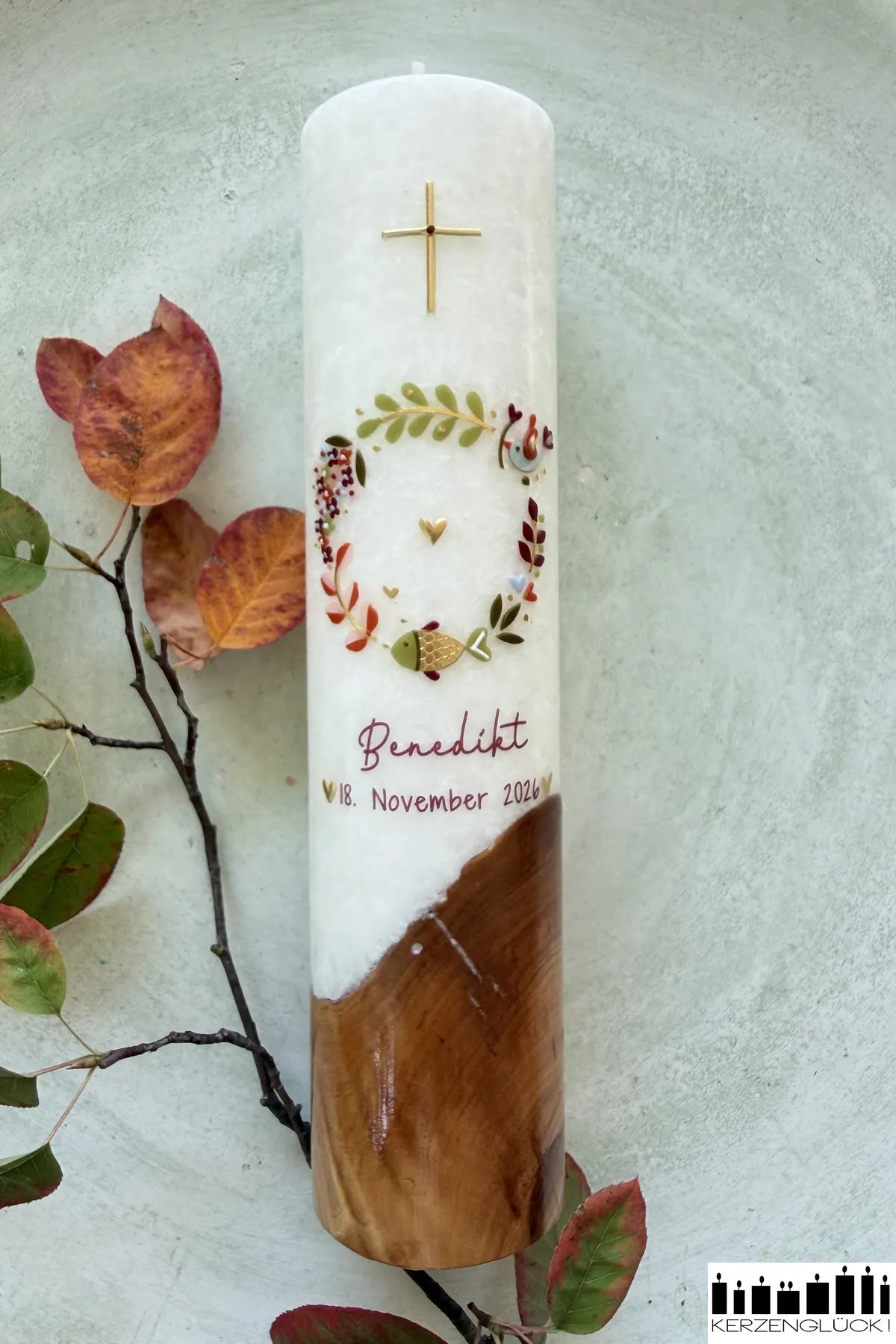 Taufkerze mit Holzelement Kranz mit Symbolen in Kürbis_Kiwi auf hellem Untergrund mit herbstlichem Zweig fotografiert